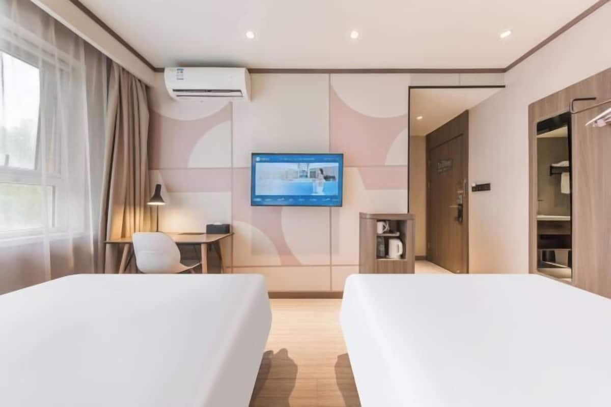 A hotel room with two beds, a desk, a chair, a TV, and a wardrobe.