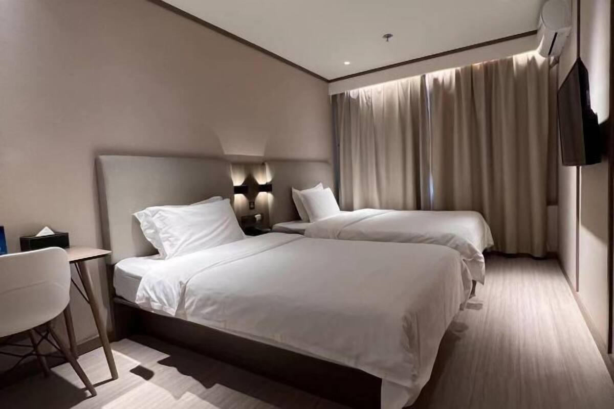 A modern hotel room with two beds, a desk, and a television.