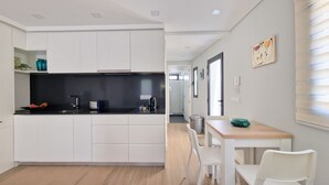 Une cuisine moderne avec des meubles blancs, un plan de travail noir et une table à manger en bois, accompagnée de chaises.
