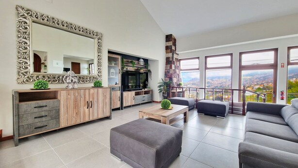 Un salon moderne avec un grand miroir, des meubles en bois, un canapé gris et un balcon offrant une vue sur la ville.