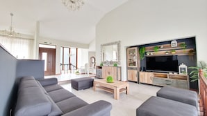 Un salon spacieux avec un grand canapé gris, une table basse en bois et un meuble TV doté d’étagères et de plantes.