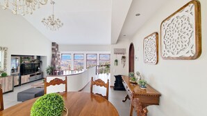 Un vaste espace dédié à la salle à manger, avec une table et des chaises en bois, un lustre et une vue sur la ville grâce à de grandes fenêtres.