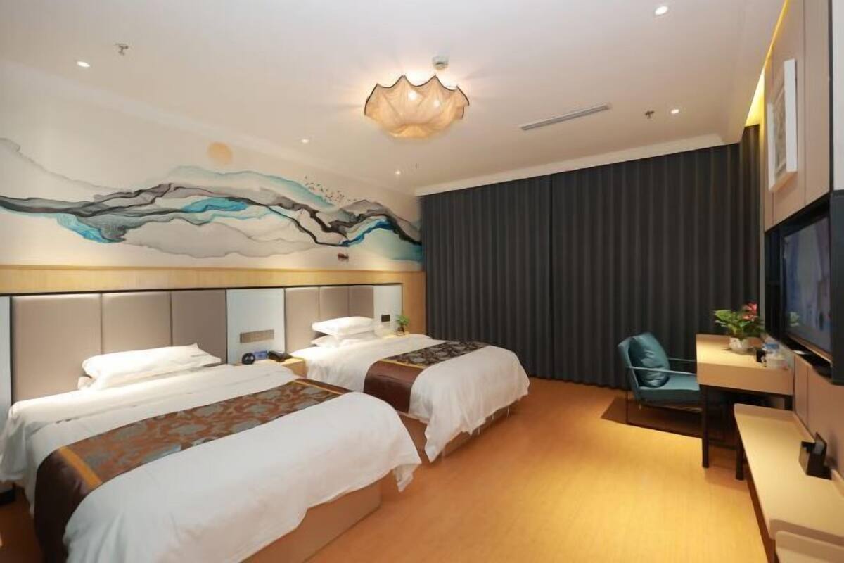 Une chambre d’hôtel avec deux lits, un bureau, une chaise, une télévision et une fresque murale.