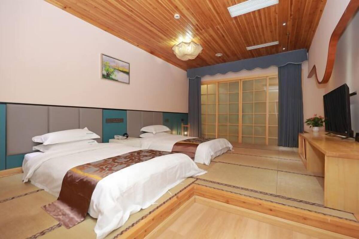 Une chambre d’hôtel avec deux lits, un plafond en bois, une grande porte-fenêtre coulissante et un téléviseur posé sur un meuble en bois.