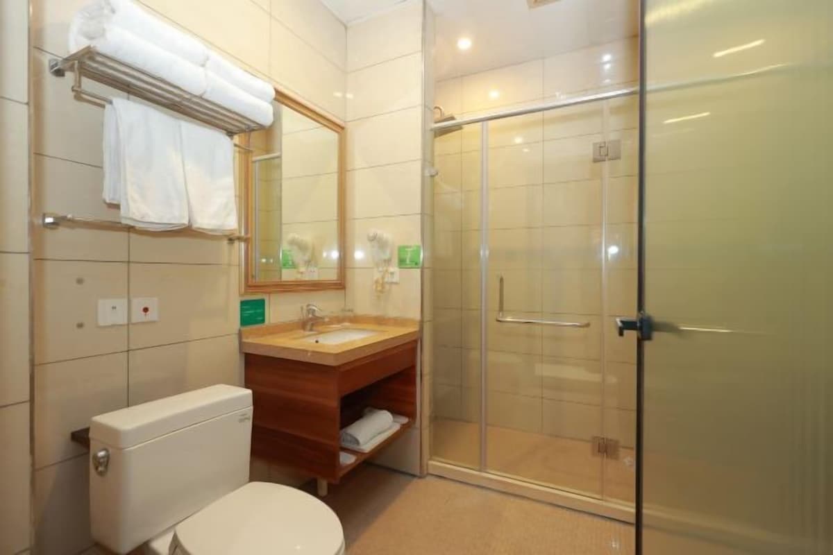 A bathroom with a toilet, sink, mirror, towel rack, and a glass-enclosed shower.