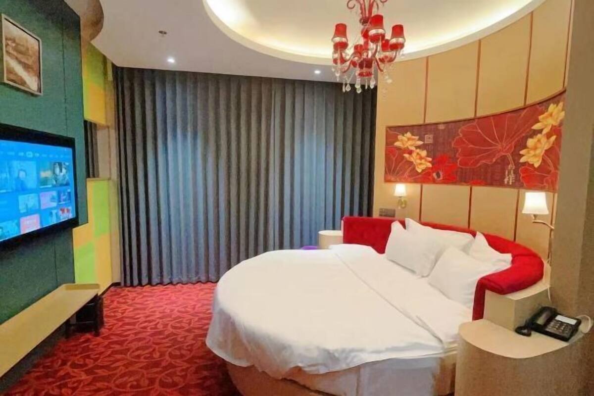 Une chambre d’hôtel avec un grand lit, une télévision, un lustre et un mur d’accent rouge.