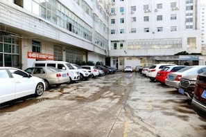 A parking lot with multiple cars, a building with a sign, and a multi-story structure in the background.