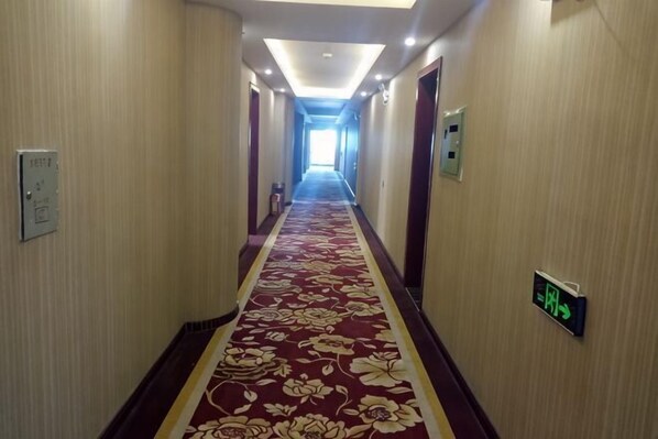 Ein Hotelgang mit rotem Teppich, Türen und einem Fluchtschild.