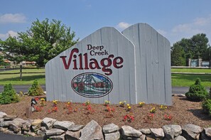 Un letrero de madera que indica Deep Creek Village, con un logotipo y un área ajardinada con flores y rocas.