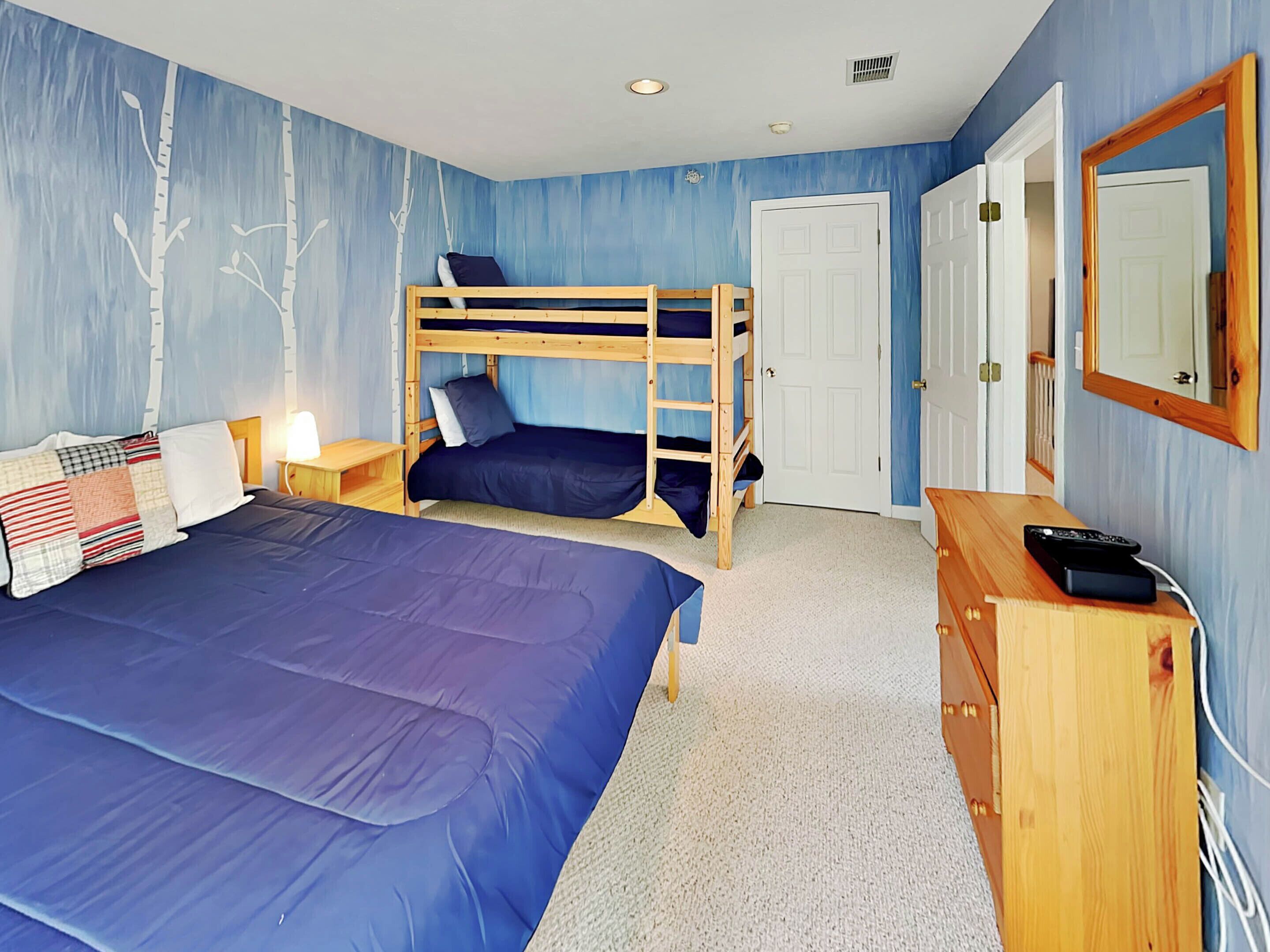 Un dormitorio con una cama litera, una cama individual, un aparador, un espejo y una puerta.