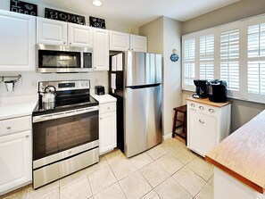 A modern kitchen with white cabinetry, stainless steel appliances, a built-in oven, microwave, and refrigerator. There is a small wooden stool and a coffee maker on the countertop.