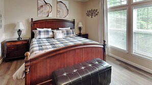 A bedroom with a wooden bed, a bench, two bedside tables, and a window with blinds. - Hillside Hideaway by Taylor Made Deep Creek (McHenry)