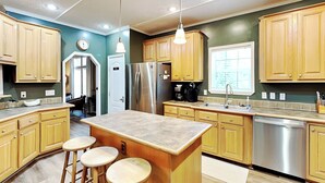 A modern kitchen with wooden cabinets, stainless steel appliances, and a central island with stools. - Hillside Hideaway by Taylor Made Deep Creek (McHenry)