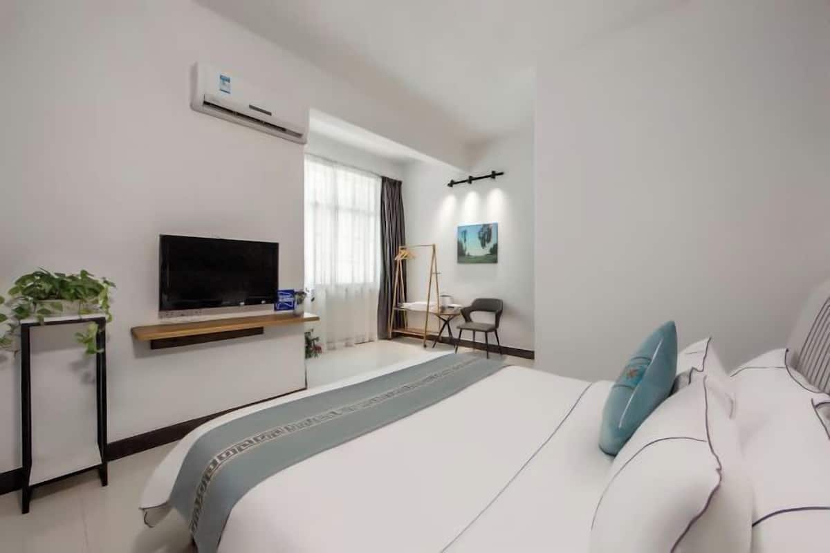 A hotel room with a bed, a TV, a desk, a chair, and a plant.