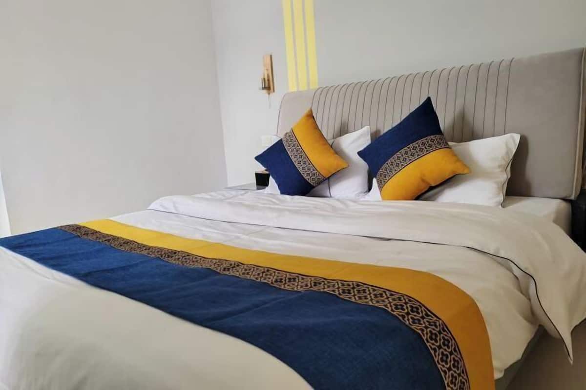 A neatly made bed with a striped bedspread, two pillows with patterned designs, and a headboard with vertical lines.