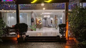 Entrada de hotel con diseño moderno, fachada de vidrio, interior bien iluminado y un camino de piedra que lleva a la entrada.