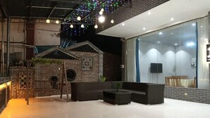 Un espacio exterior con mesas y sillas, una pared de ladrillo, un ventanal y luces colgantes.