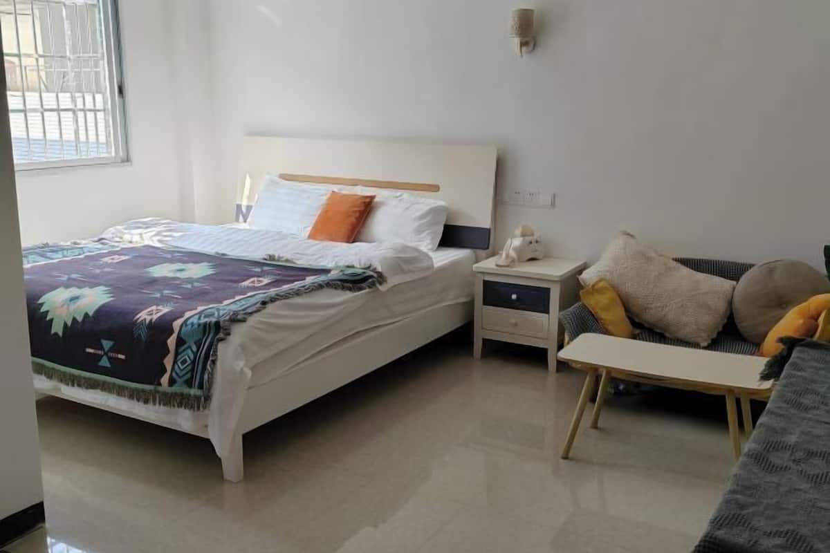 A bedroom with a bed, bedside tables, a nightstand, a sofa, and a window with bars.