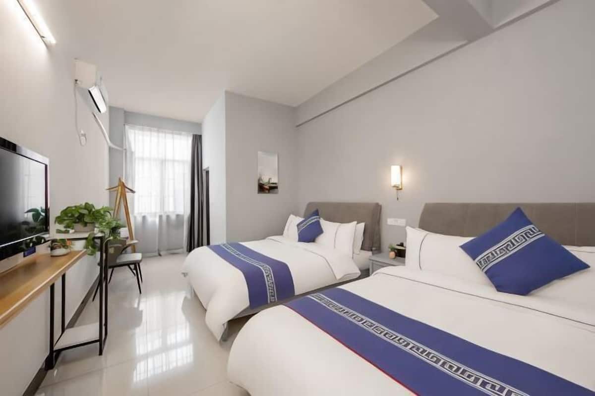 A hotel room with two beds, a desk with a TV, a chair, and a window with curtains.