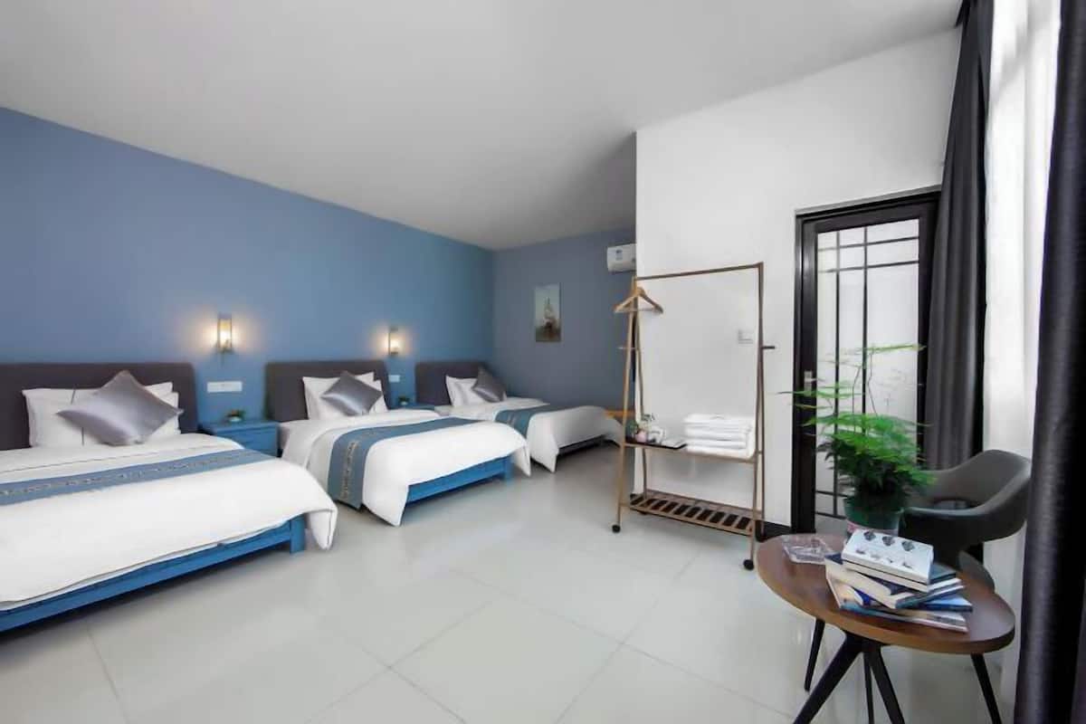 A hotel room with two beds, a small table with books, a plant, and a window with curtains.