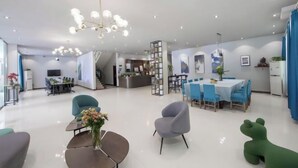 Un amplio vestíbulo de hotel con zona de comedor central, mostrador de recepción y una escalera que conduce a los pisos superiores.