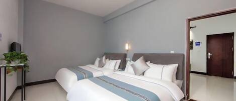 A hotel room with two beds, a bedside table with a plant, a mirror, and a door.