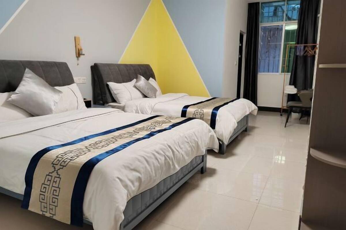 A hotel room with two beds, a yellow accent wall, and a window with curtains.
