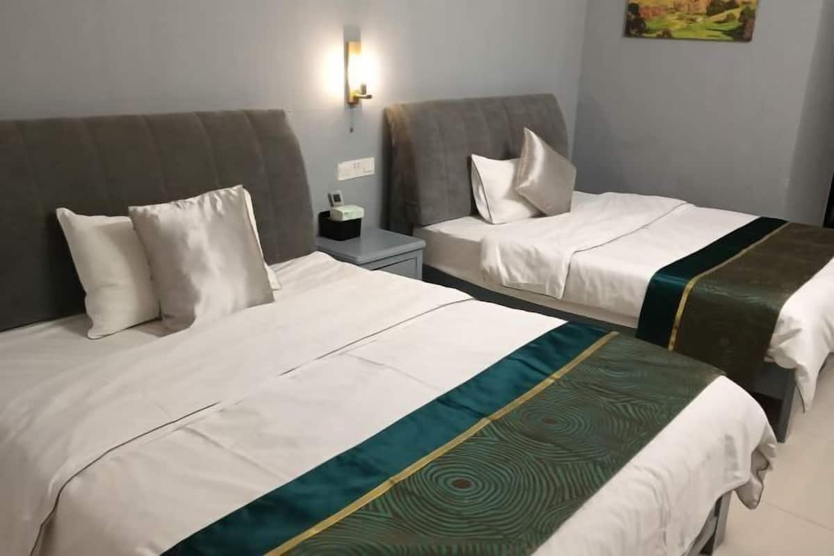 Two beds with white linens and green accents, a nightstand with a lamp, and a painting on the wall.