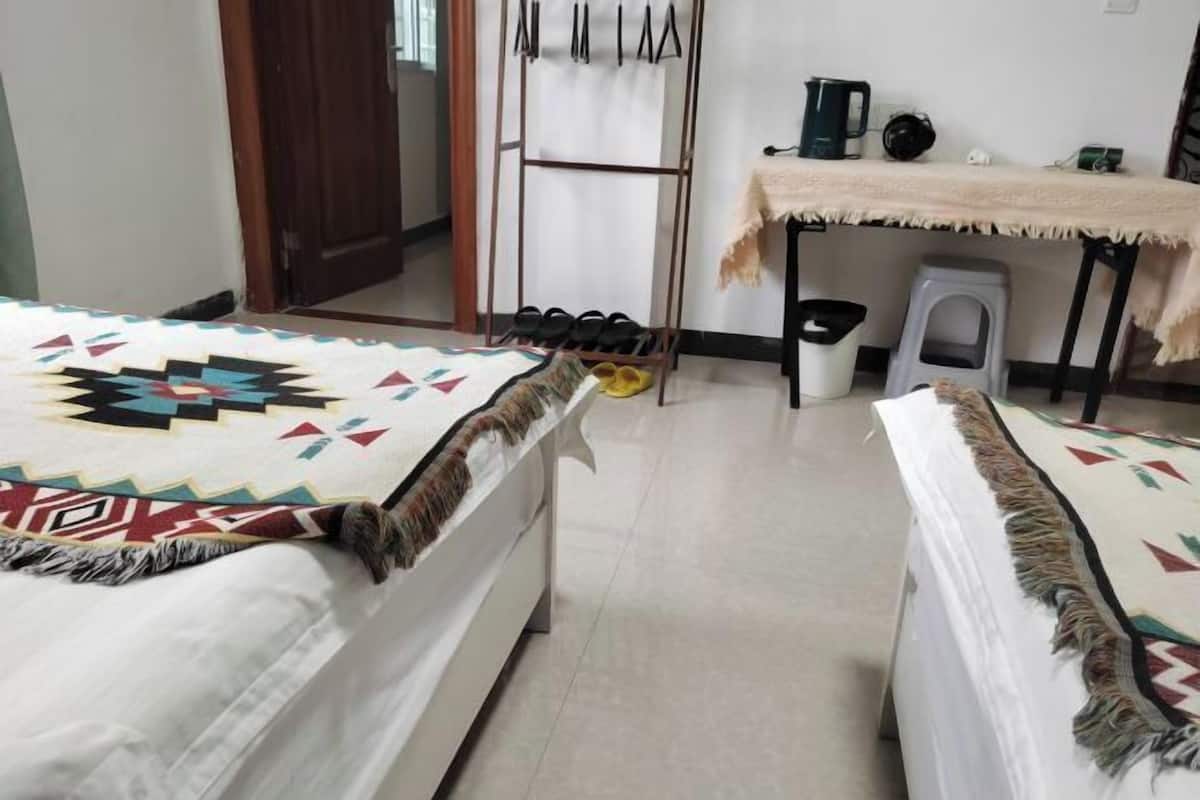 A hotel room with two beds, a small table with a coffee maker, a shoe rack, and a trash bin.