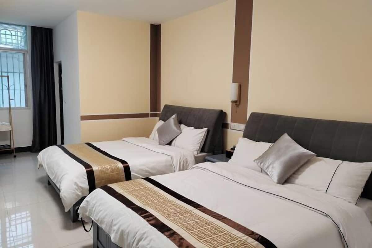 A hotel room with two beds, a nightstand, a lamp, and a window with curtains.