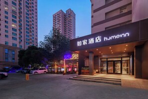 Entrada de hotel con un letrero llamativo, una zona de estacionamiento y edificios circundantes.