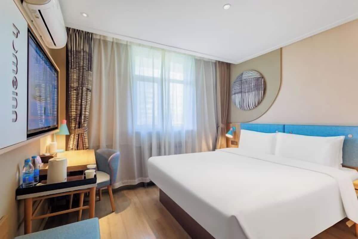 Une chambre d’hôtel avec un lit, un bureau et une chaise, une télévision et une fenêtre avec des rideaux.