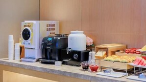 Morgenmadsbuffet med kaffemaskiner, en drikkemaskine og et udvalg af mad, herunder bagværk og frugt.
