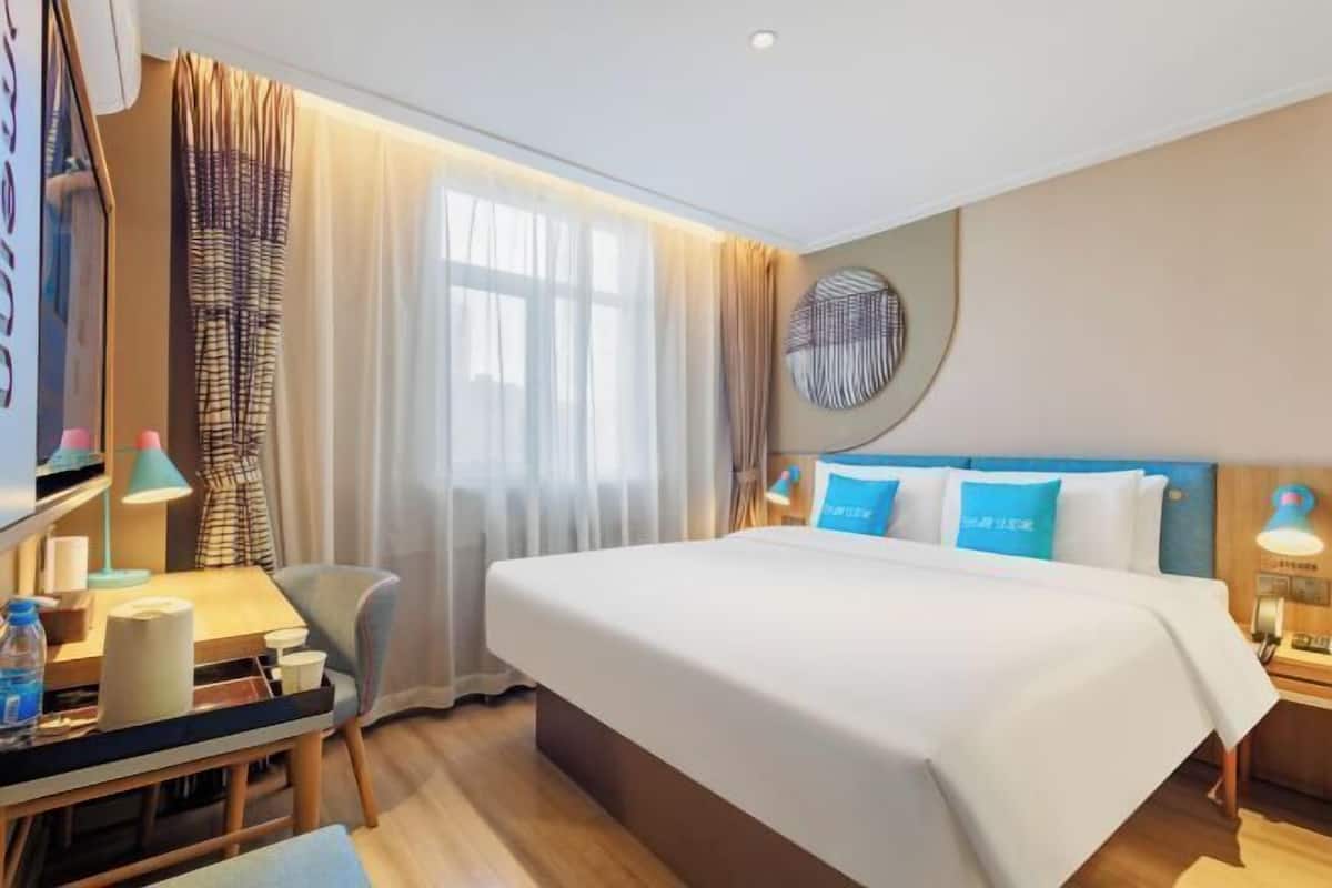 Une chambre d’hôtel avec un lit, un bureau, une chaise, une télévision et une fenêtre avec des rideaux.