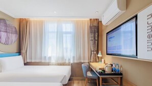 Et hotelværelse med to senge, et skrivebord med lampe, et fjernsyn og et stort vindue med gardiner.