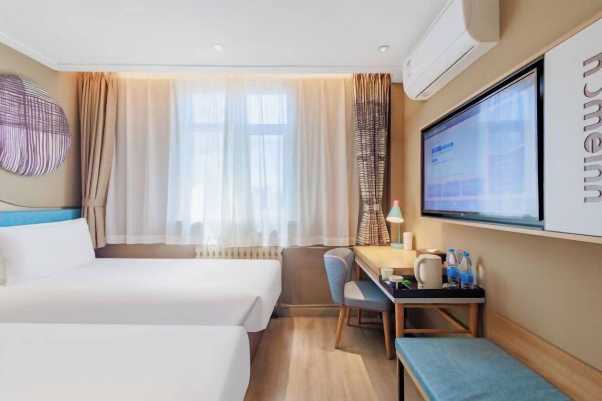 Une chambre d’hôtel avec deux lits, un bureau avec une lampe, une télévision et une grande fenêtre avec des rideaux.
