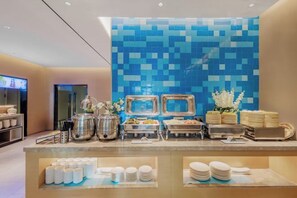 Montaje de bufé con diferentes recipientes de comida, una pared con azulejos y una pantalla de televisión.