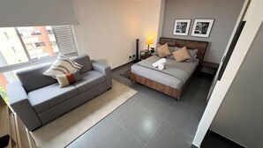 Un dormitorio moderno con un sofá gris, un cabecero de madera y una mesita de noche con lámpara.