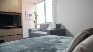Un dormitorio moderno con una cama, un sofá gris, un televisor, un mapa del mundo y una ventana con persianas.