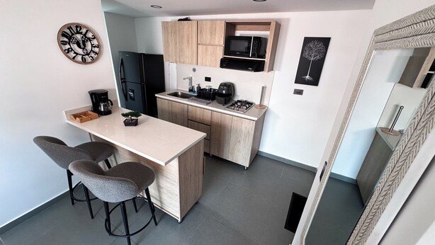 Una cocina compacta con una isla central, taburetes de bar, un microondas y un refrigerador.