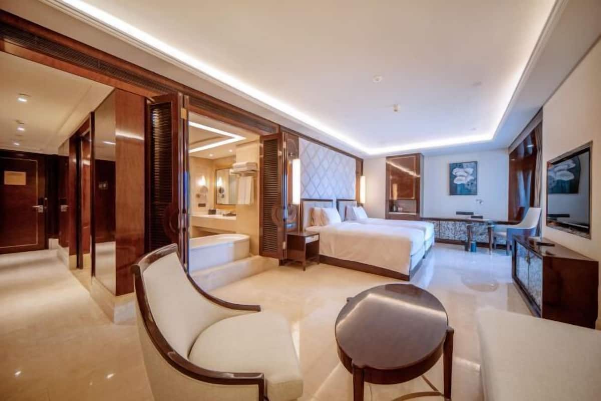A hotel room with a large bed, a sitting area with a chair, a desk, and a TV.