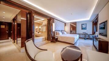 A hotel room with a large bed, a sitting area with a chair, a desk, and a TV.