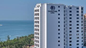 A tall hotel building with a clear view of the ocean and palm trees.
