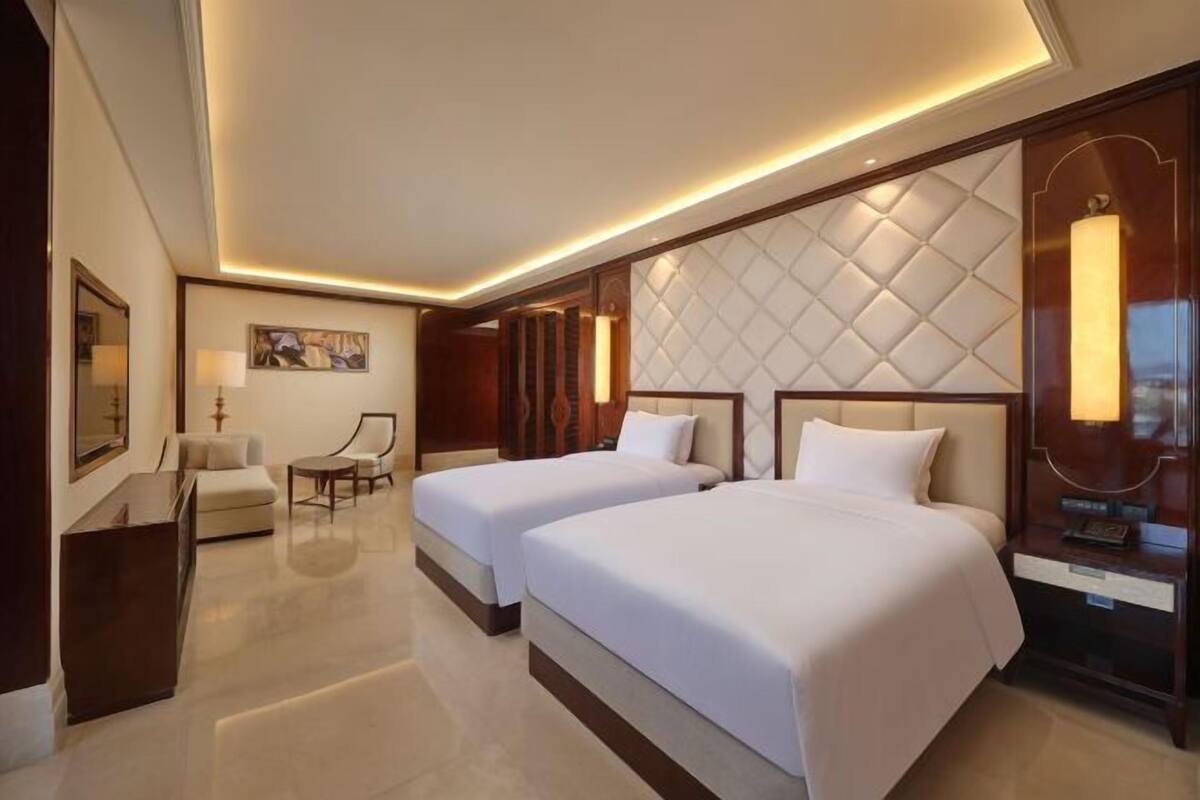 A hotel room with two beds, a desk, a chair, and a decorative wall panel.