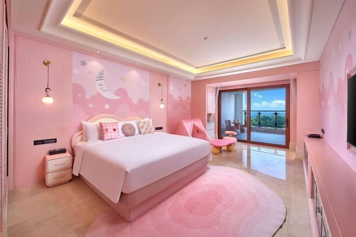 A pink-themed bedroom with a large bed, a nightstand, a dresser, and a TV.