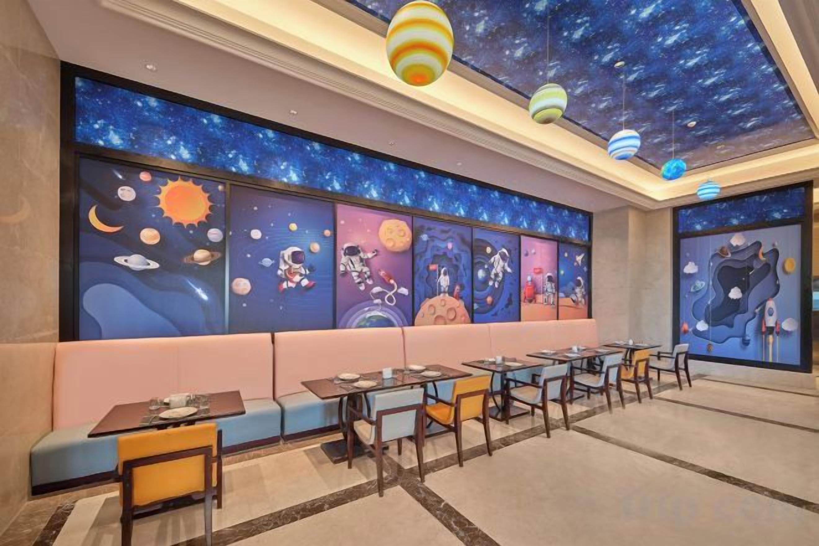 Een restaurant met een muurschildering over het thema ruimte, zitplaatsen en hangende bolvormige lampen.