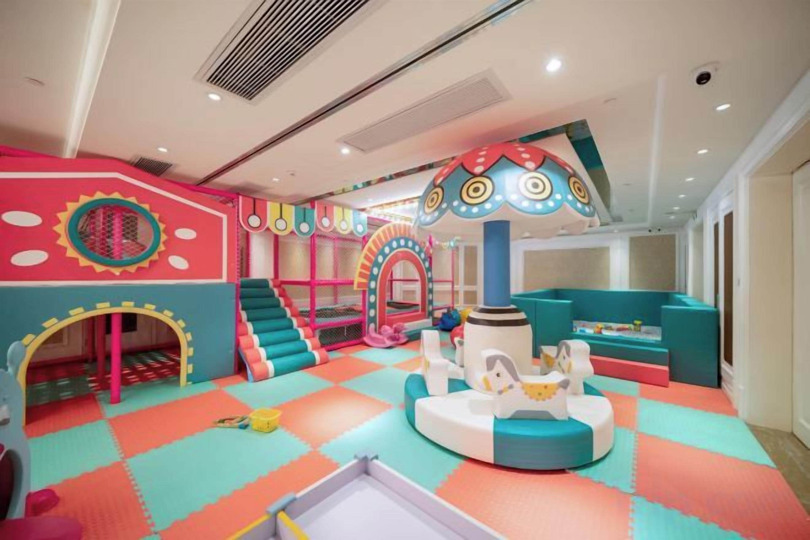 A children's play area with colorful play structures, a slide, and a soft play floor.