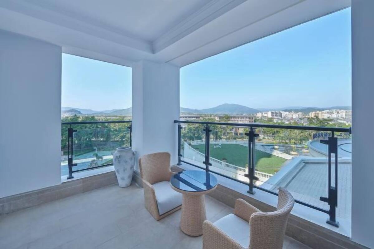 A balcony with wicker furniture, a vase, and a view of a cityscape and mountains.