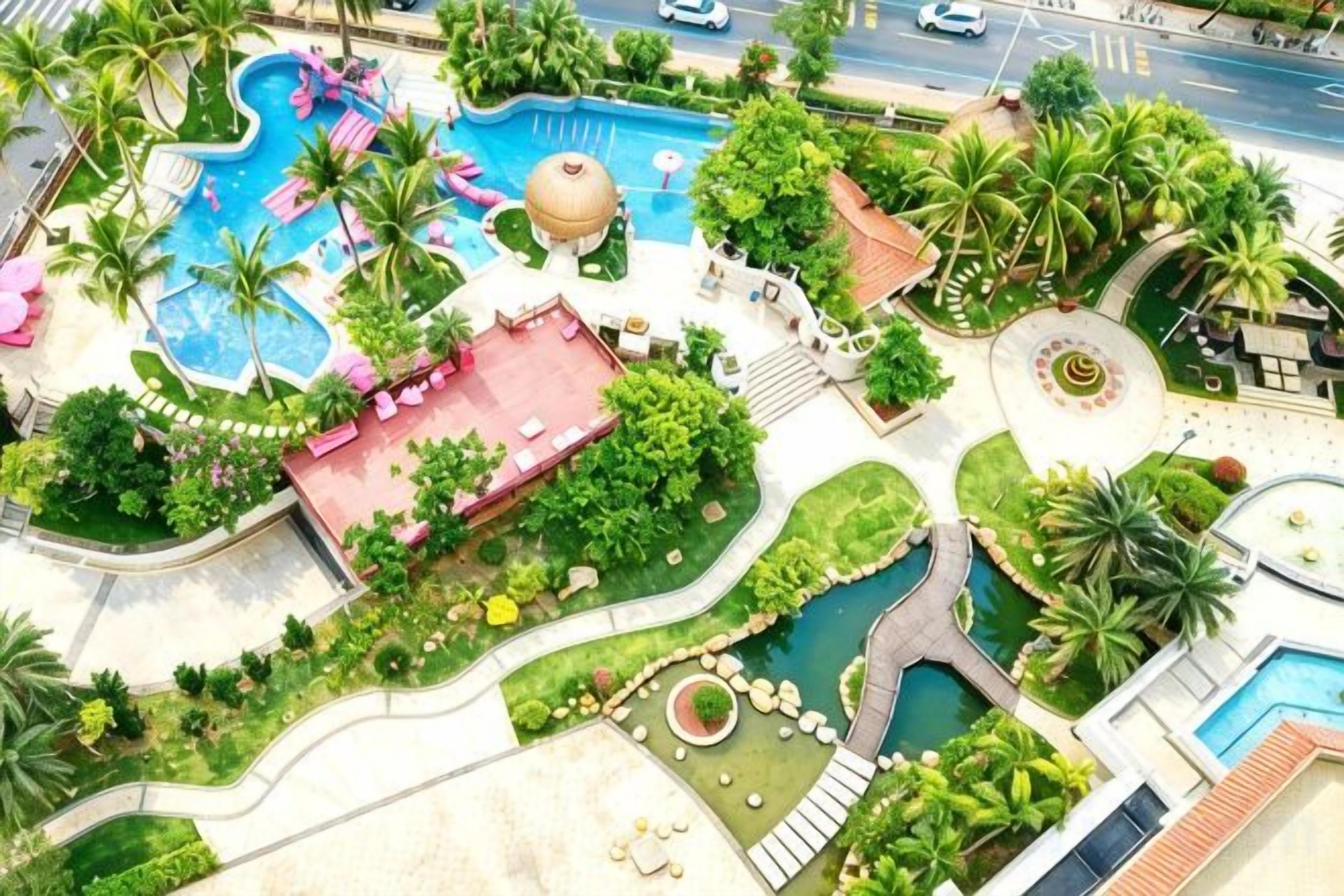 Un complexe hôtelier doté d’une piscine, de palmiers et d’un bâtiment au toit rouge.