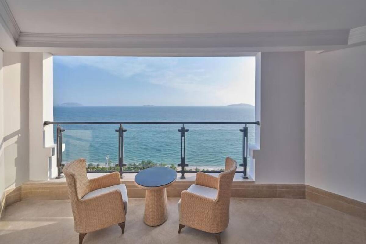 A balcony with two wicker chairs and a small round table, overlooking a body of water and distant land.